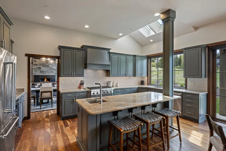 Kitchen featuring wood-finish flooring, custom cabinetry with a range hood, stainless steel appliances, a center island with bar seating, and skylights