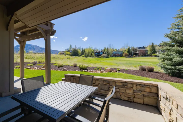 Covered patio with concrete flooring and a stone-clad retaining wall, overlooking a landscaped yard and distant mountainous terrain