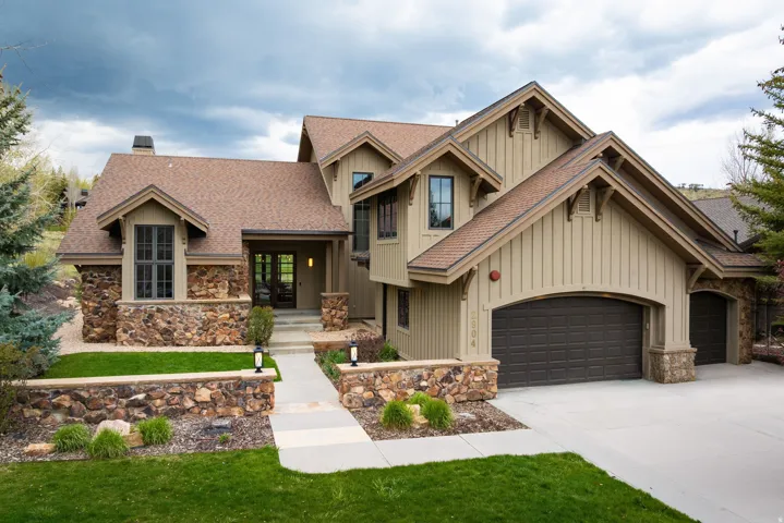 Craftsman-style exterior featuring stone accents, vertical wood siding, a covered entry, an arched garage door, and a paved driveway