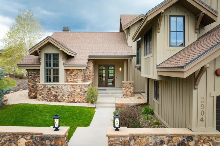 Stone and board-and-batten exterior featuring a prominent gabled window, a covered entryway with double doors, stone columns, and a concrete pathway