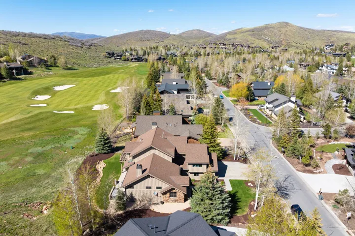Residential community with golf course frontage, mature trees, paved streets, mountain backdrop, and varying architectural styles
