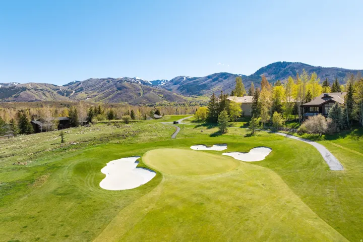 Expansive golf course green with sand traps, surrounded by mature trees and natural landscaping