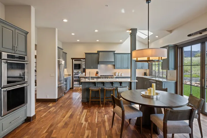 Gourmet kitchen and dining area featuring rich wood-finish flooring, custom cabinetry, stainless steel double ovens, and expansive sliding glass doors
