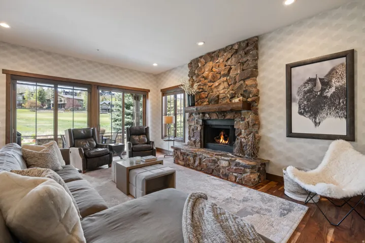 Living room featuring a stone fireplace with a wood mantle, large windows, wood-finish flooring, and recessed lighting