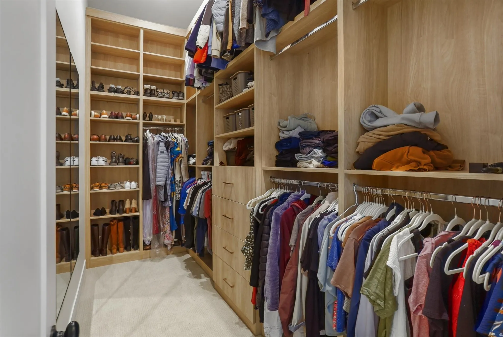 Custom walk-in closet featuring light wood-finish cabinetry, extensive shelving, built-in drawers with modern hardware, and multiple hanging rods