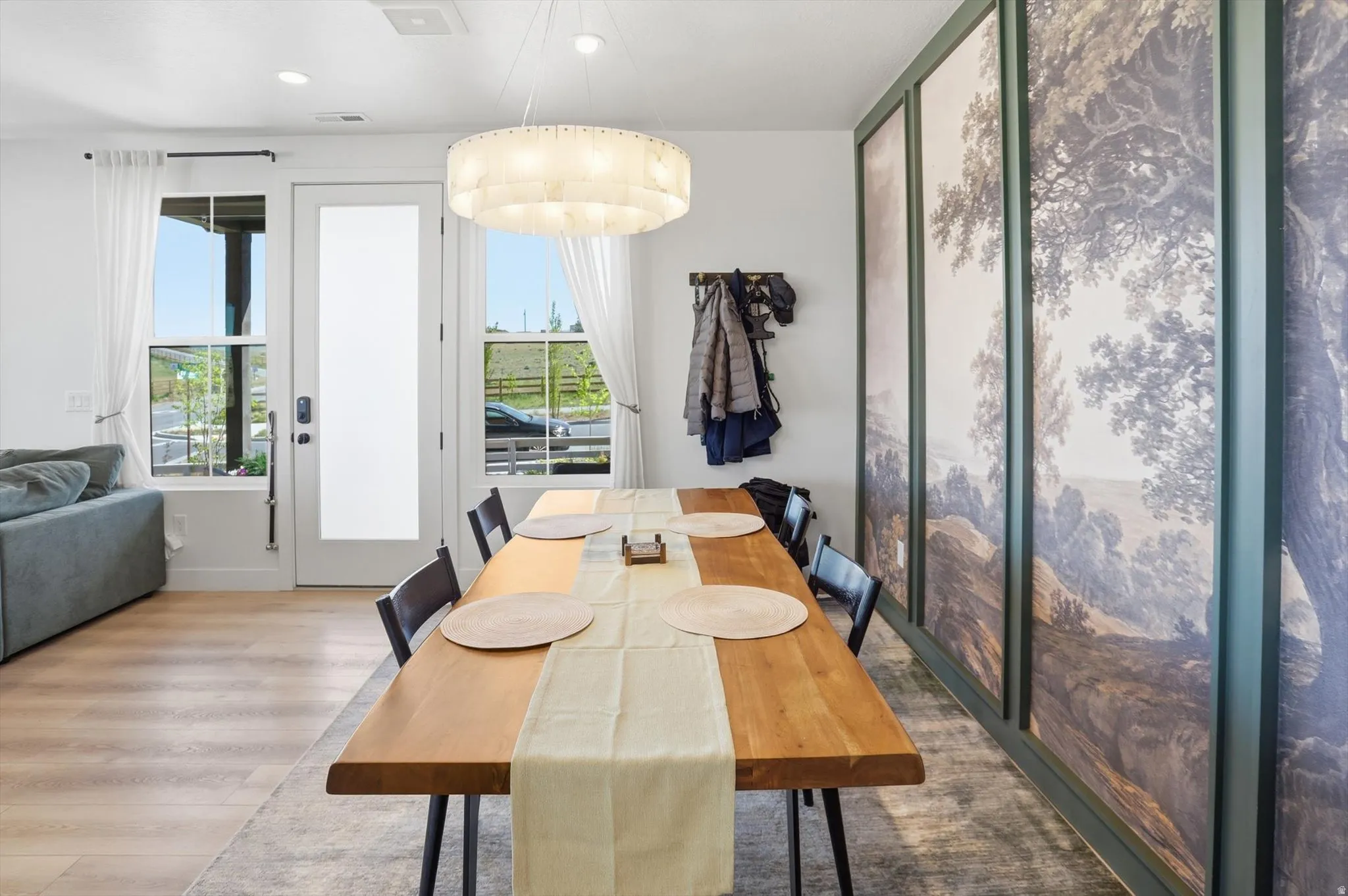 Dining area featuring wood-finish flooring, a contemporary chandelier, and a wall of framed landscape art