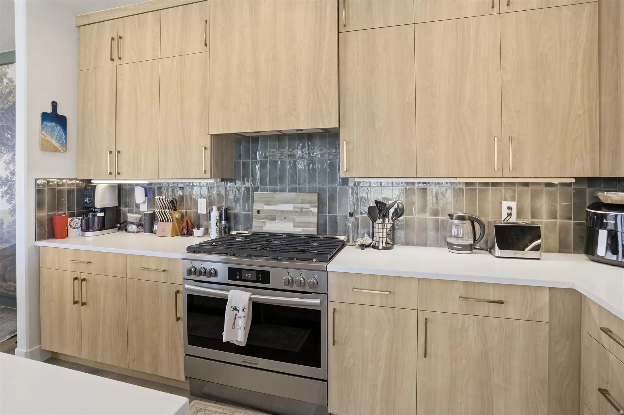 Modern kitchen featuring light wood-finish cabinetry, white countertops, and a tiled backsplash