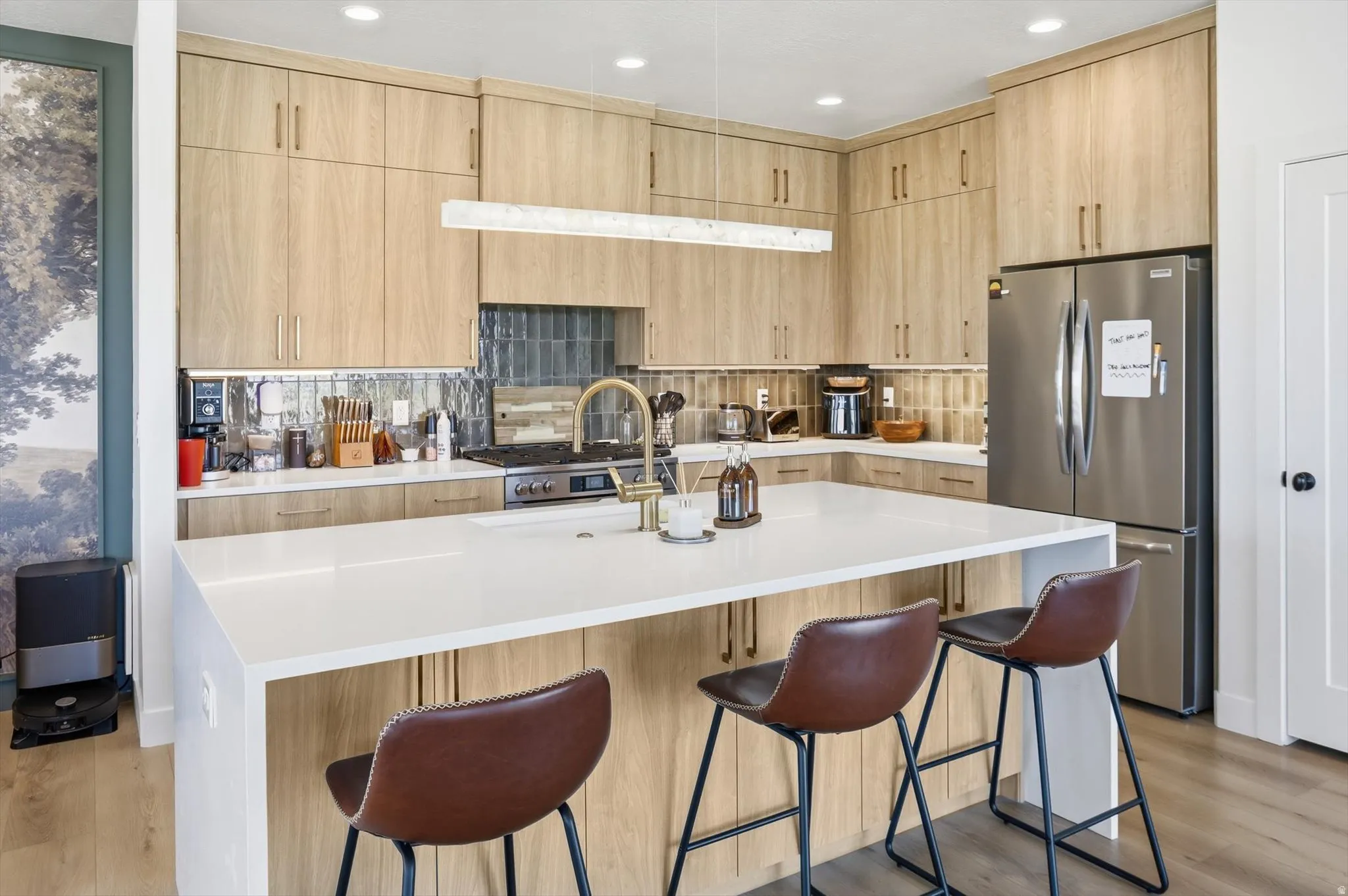 Modern kitchen featuring light wood-finish cabinetry, a large center island with a white countertop, and stainless steel appliances