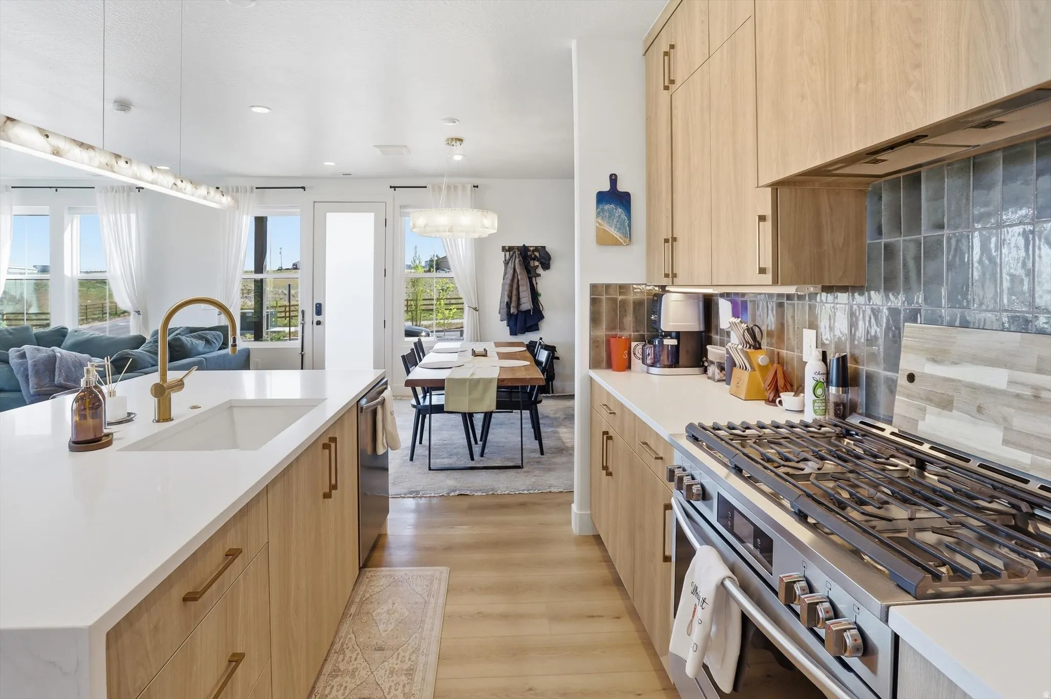 Spacious kitchen featuring light wood-finish cabinetry, a large white countertop island with an undermount sink, and stainless steel appliances including a gas range