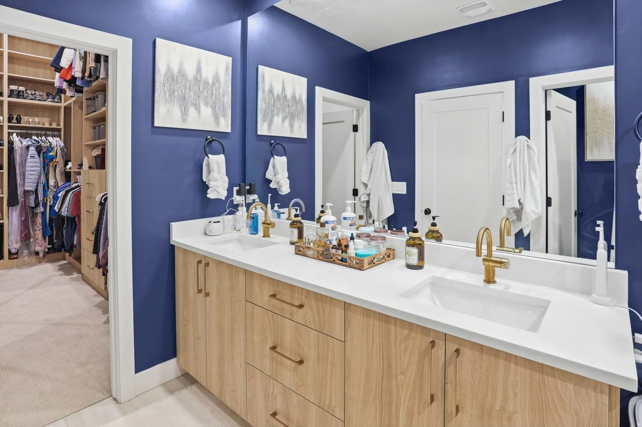 Dual vanity with light wood-finish cabinetry, white countertops, and gold-toned fixtures