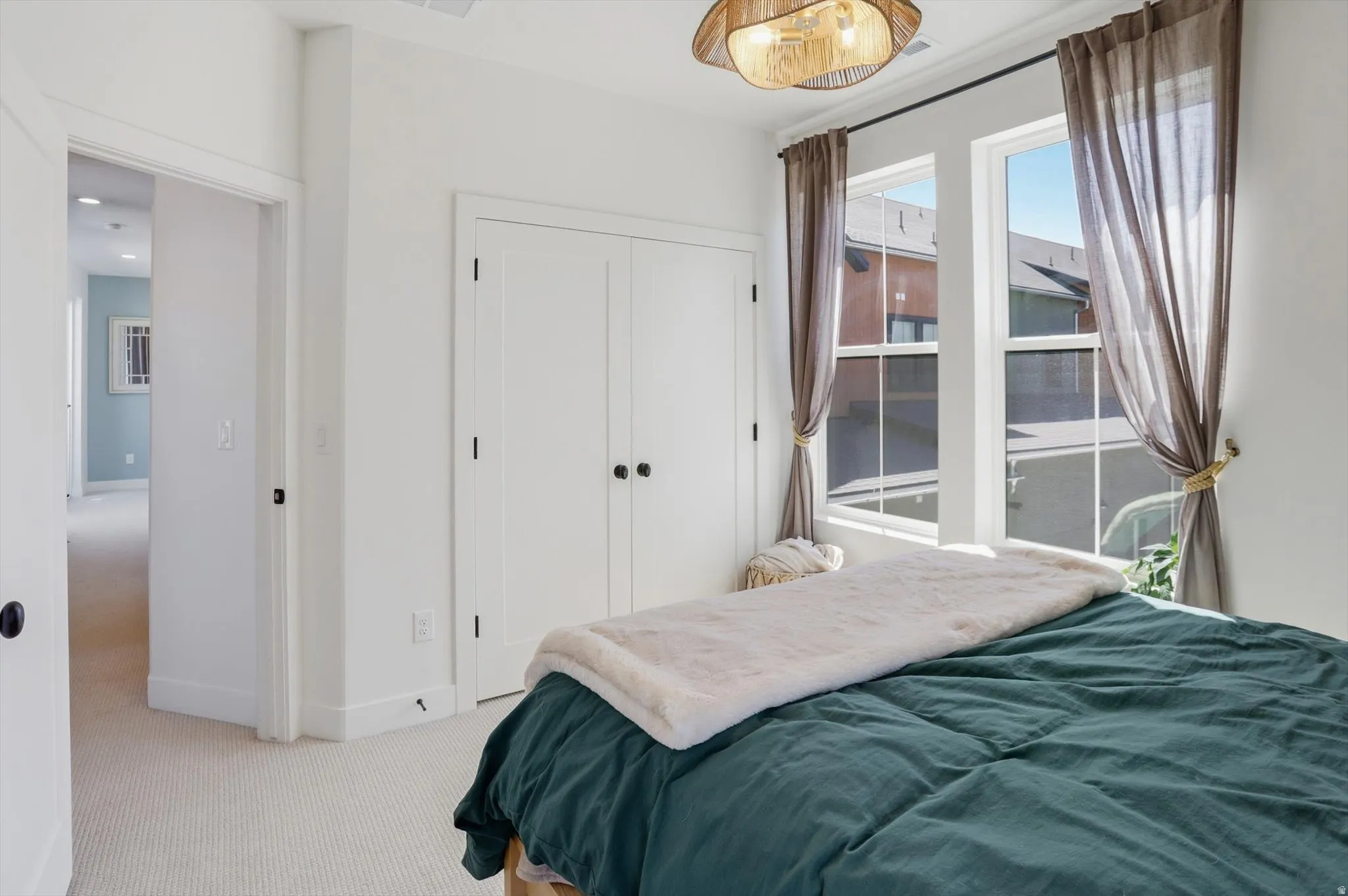 Bedroom featuring two large windows with sheer drapes, a dual-door closet with dark hardware, and light-colored carpeting