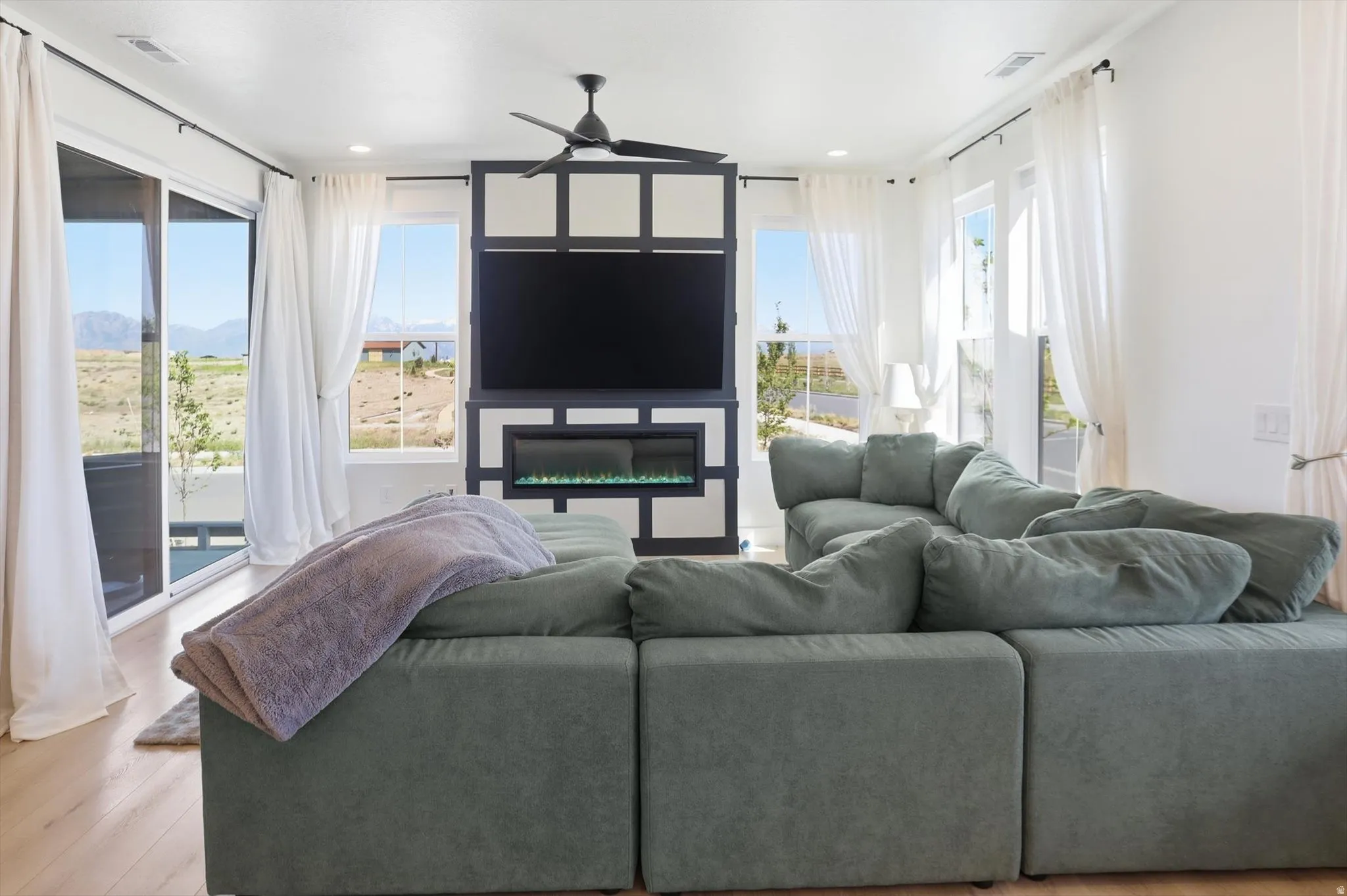 Open living area featuring a built-in media center with an electric fireplace, light wood-finish flooring, recessed lighting, and a ceiling fan