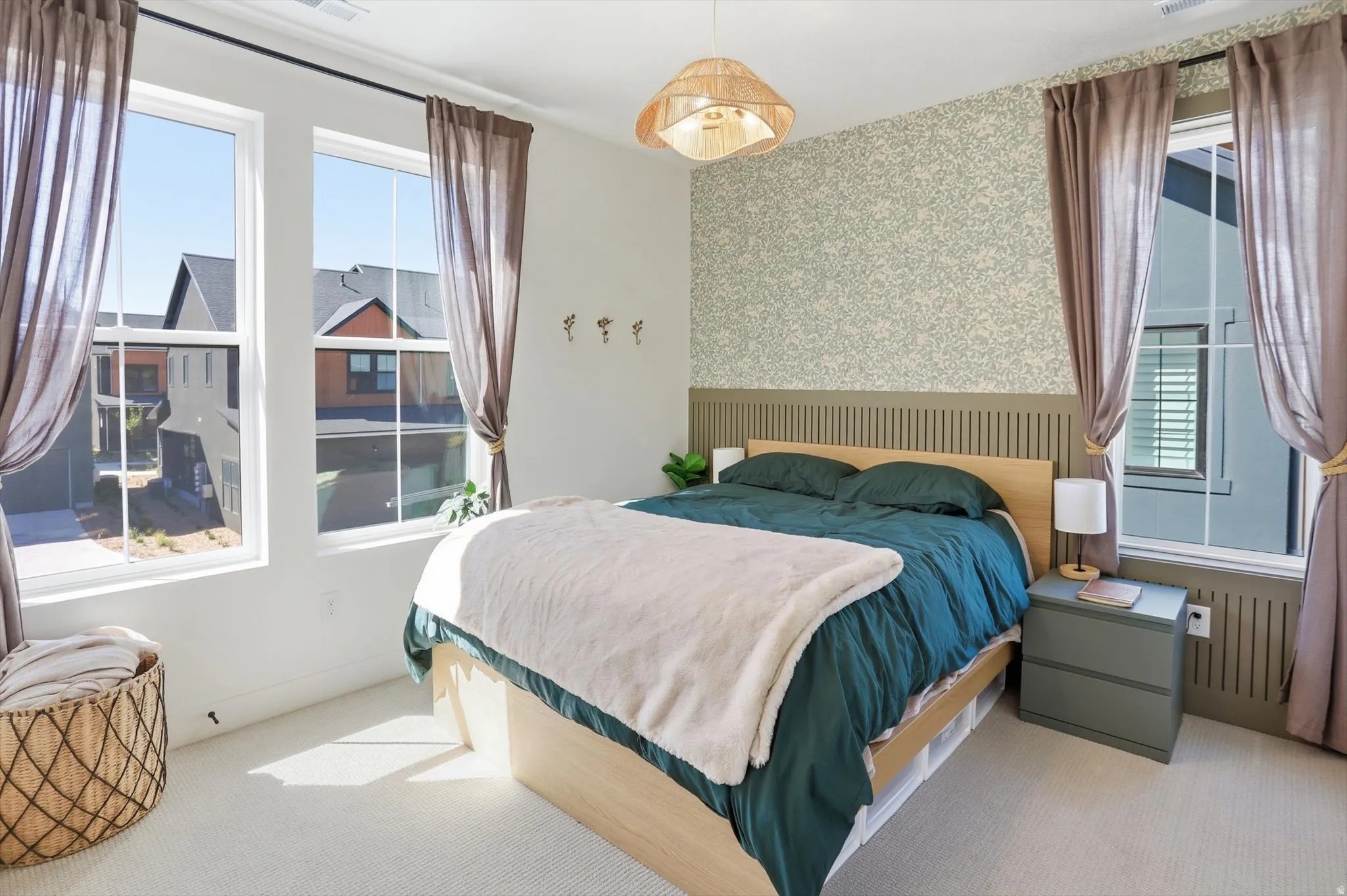 Carpeted bedroom featuring a textured accent wall, two large windows, and a slatted wood panel wainscoting