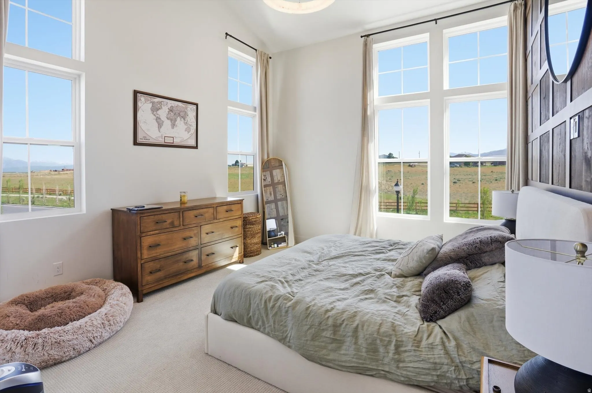 Bright room with high ceilings, featuring multiple large windows, a wood-finish dresser, and light-colored carpeting