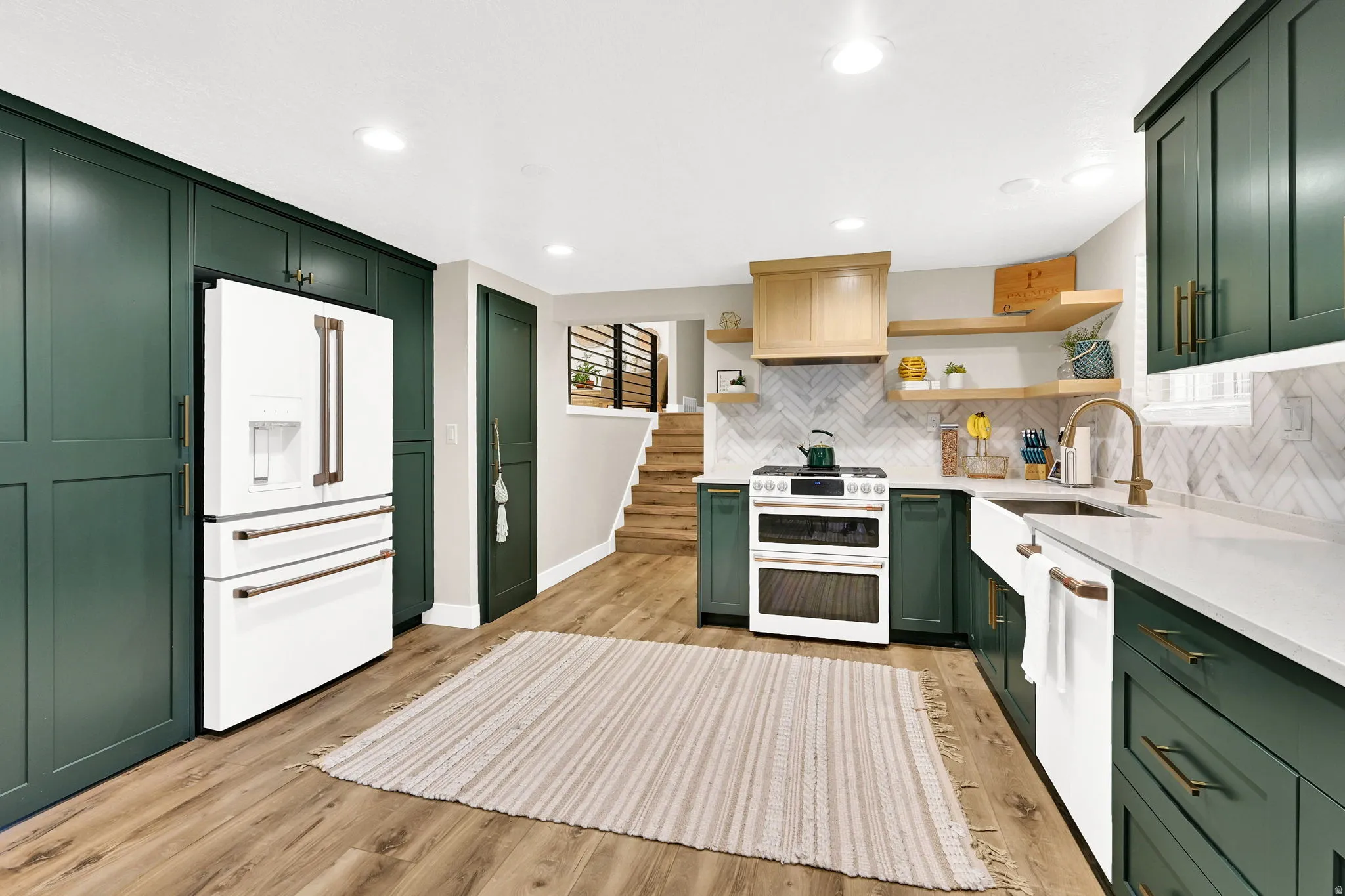 Modern kitchen featuring dark green cabinetry, white appliances, wood-finish flooring, white countertops, and a white subway tile backsplash. "Hidden pantry" door is located next to the fridge.  And GE Cafe appliances are included.