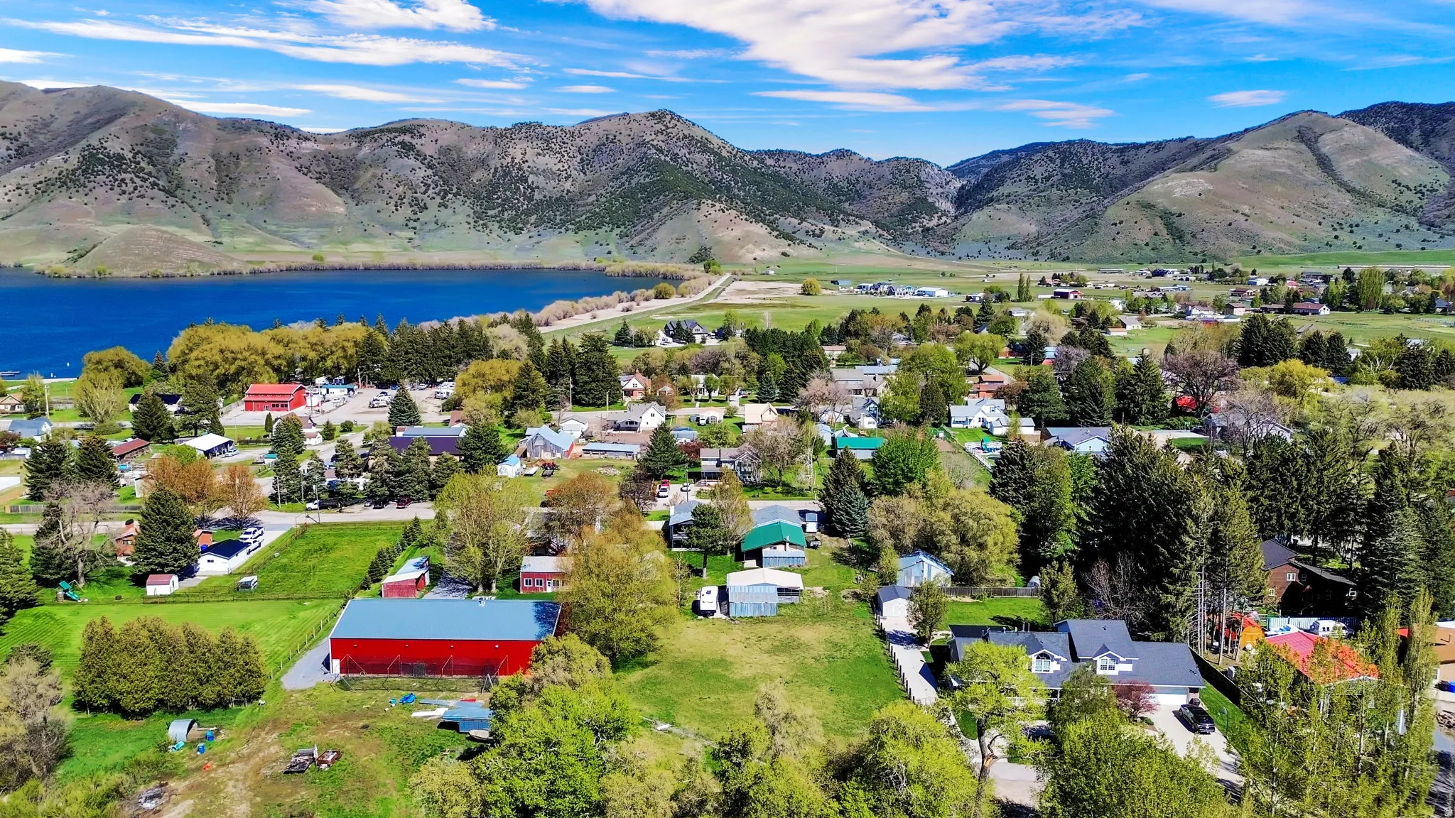 Expansive rural landscape featuring a large body of water, distant mountains, a collection of residential properties, verdant trees, and open green spaces