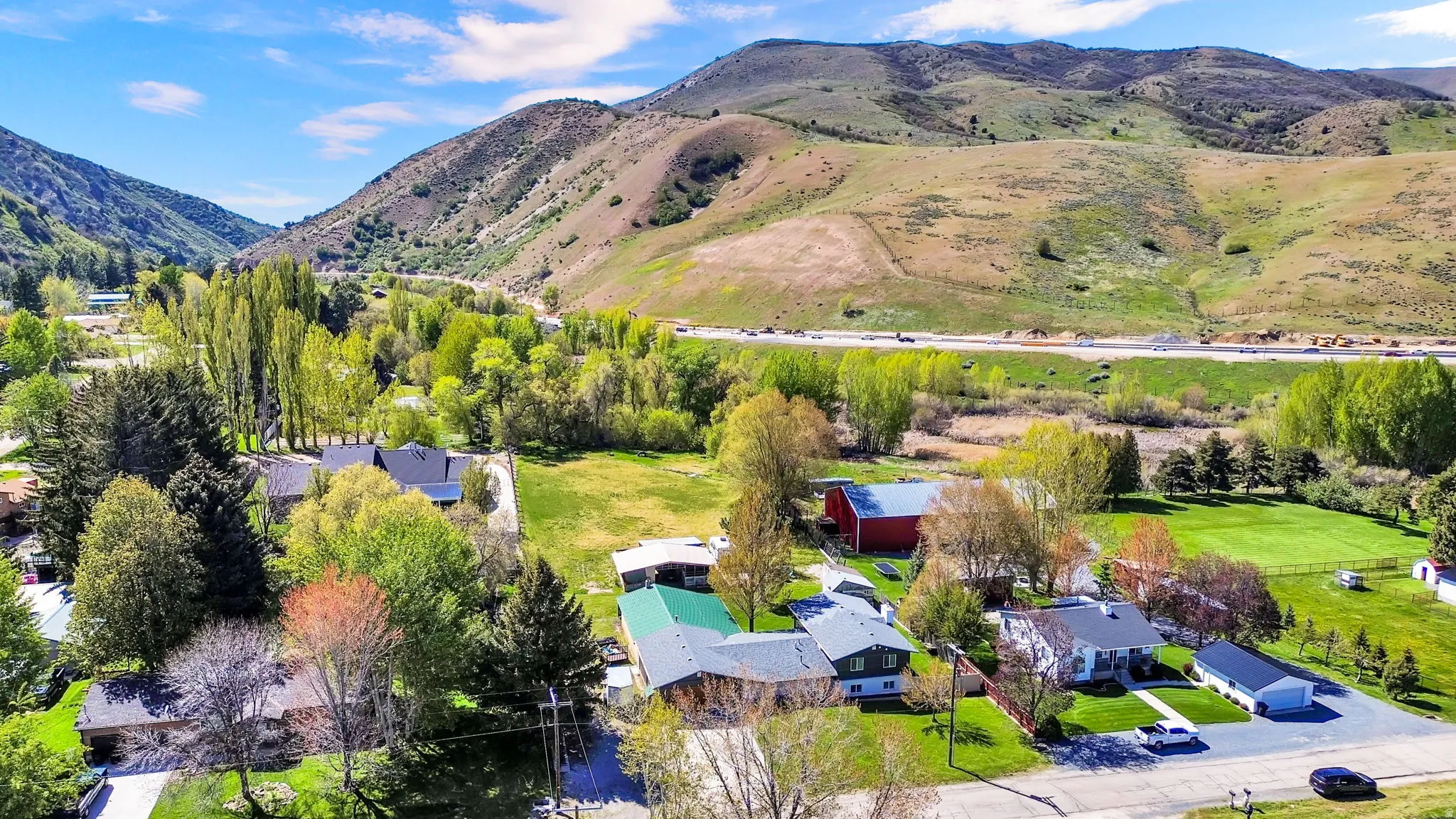 Mountain valley setting featuring residential properties, expansive green spaces, mature trees, and distant highway access