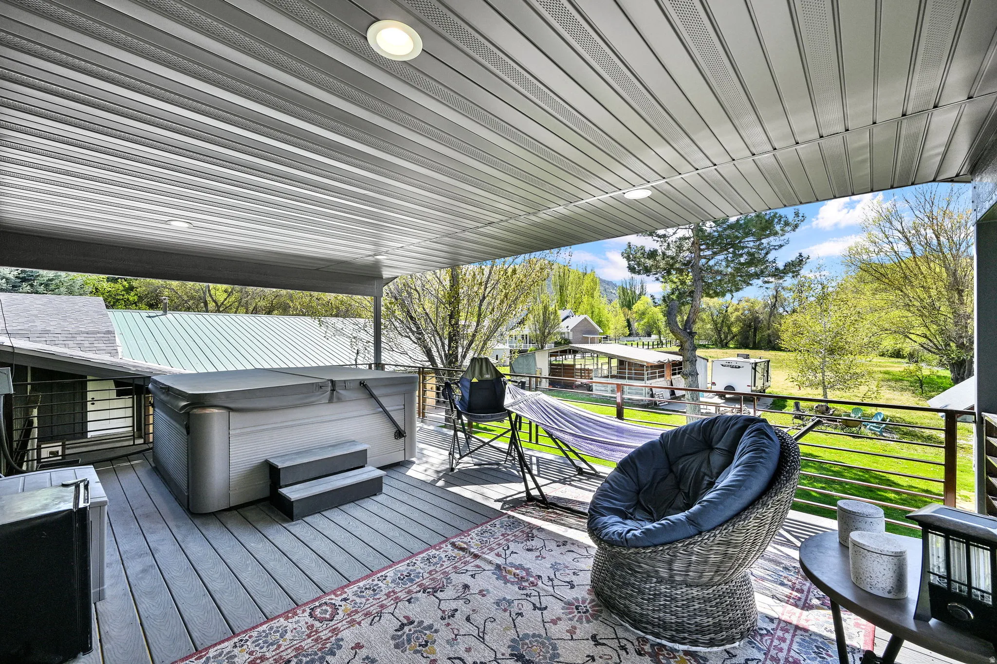 Covered outdoor deck featuring a hot tub, recessed lighting, and a horizontal slatted railing. Private entrance from primary suite.