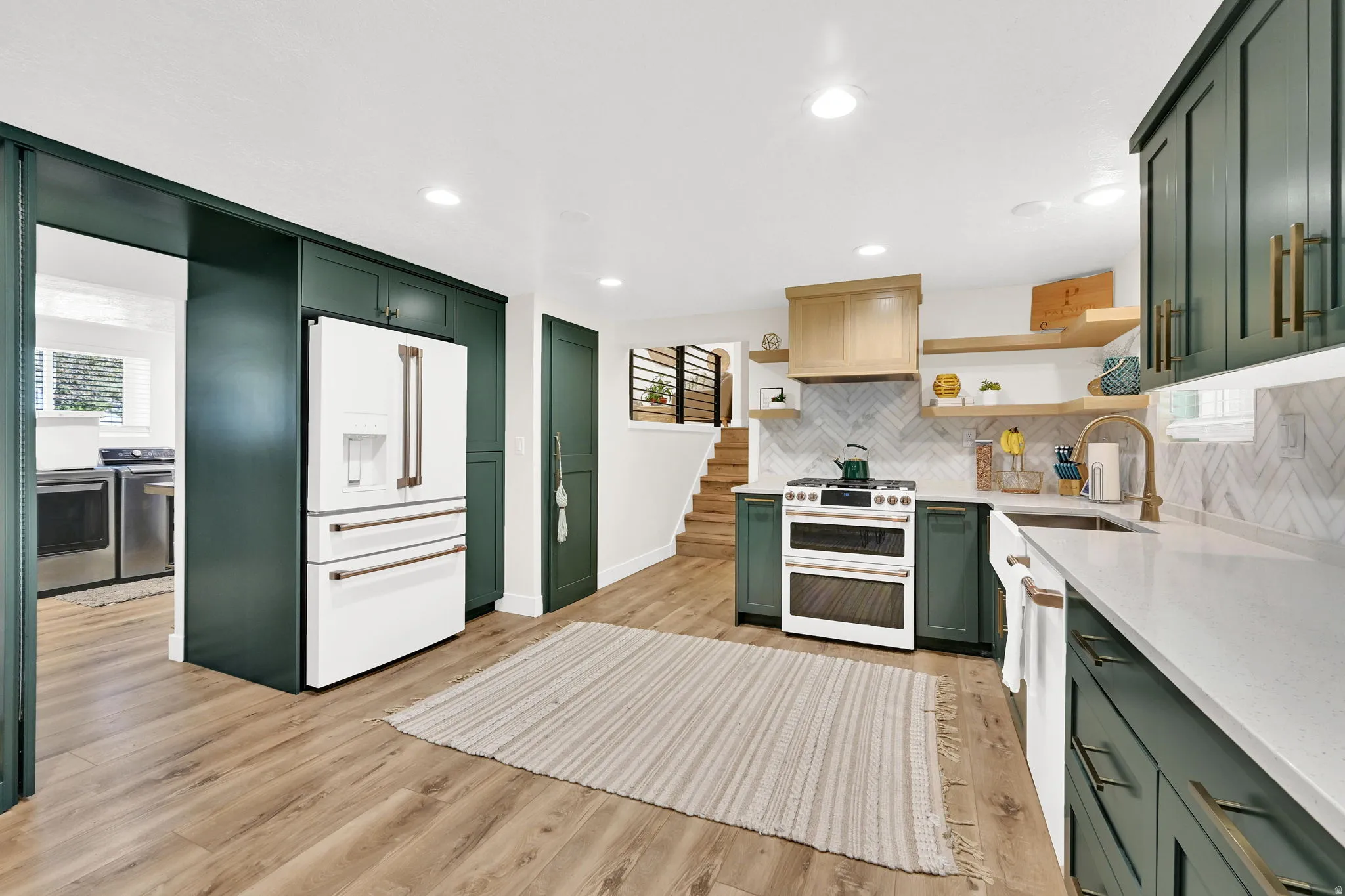 Modern kitchen featuring wood-finish flooring, dark green cabinetry, white countertops, and a white tile backsplash.  "Hidden pantry" door is located next to the fridge. And GE Cafe appliances are included.