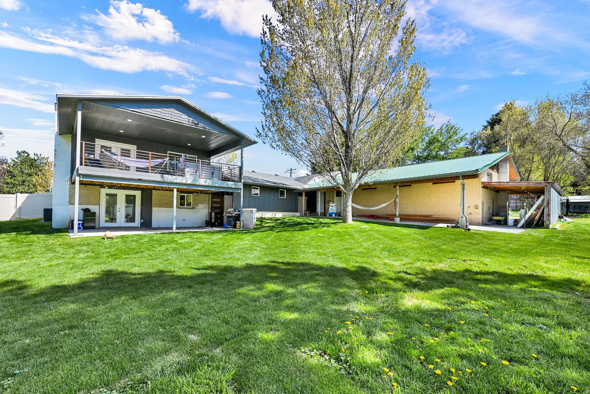 Expansive green lawn with mature tree, featuring a multi-level exterior with covered balcony, covered patio with French doors, and an additional single-story structure with covered exterior space