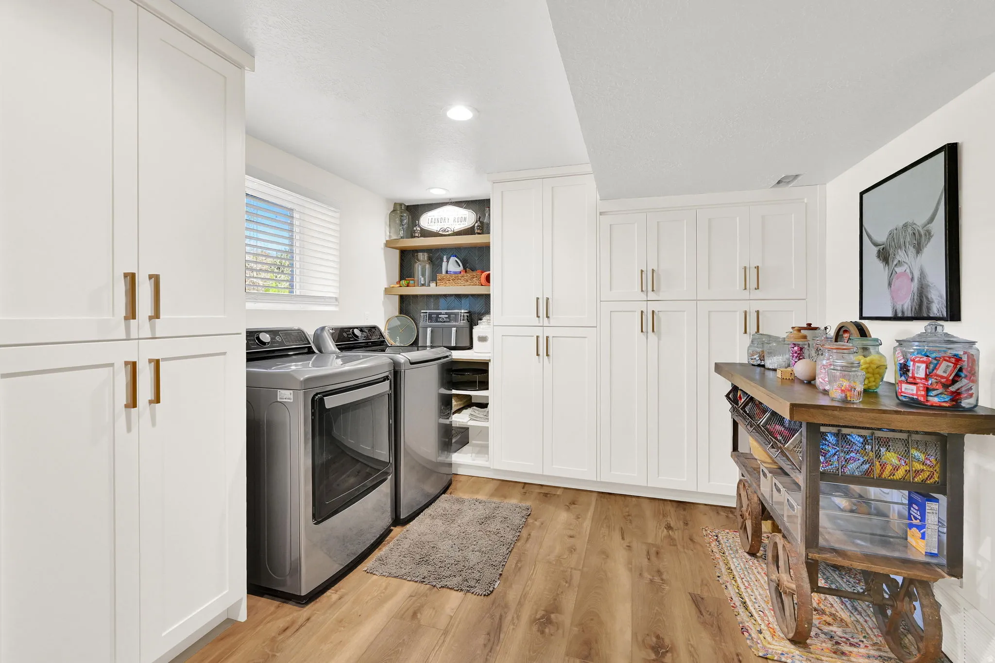 Hidden butler pantry with laundry area featuring wood-finish flooring, white cabinetry with gold-tone hardware, dark subway tile backsplash, and stainless steel appliances (wine cooler is included)