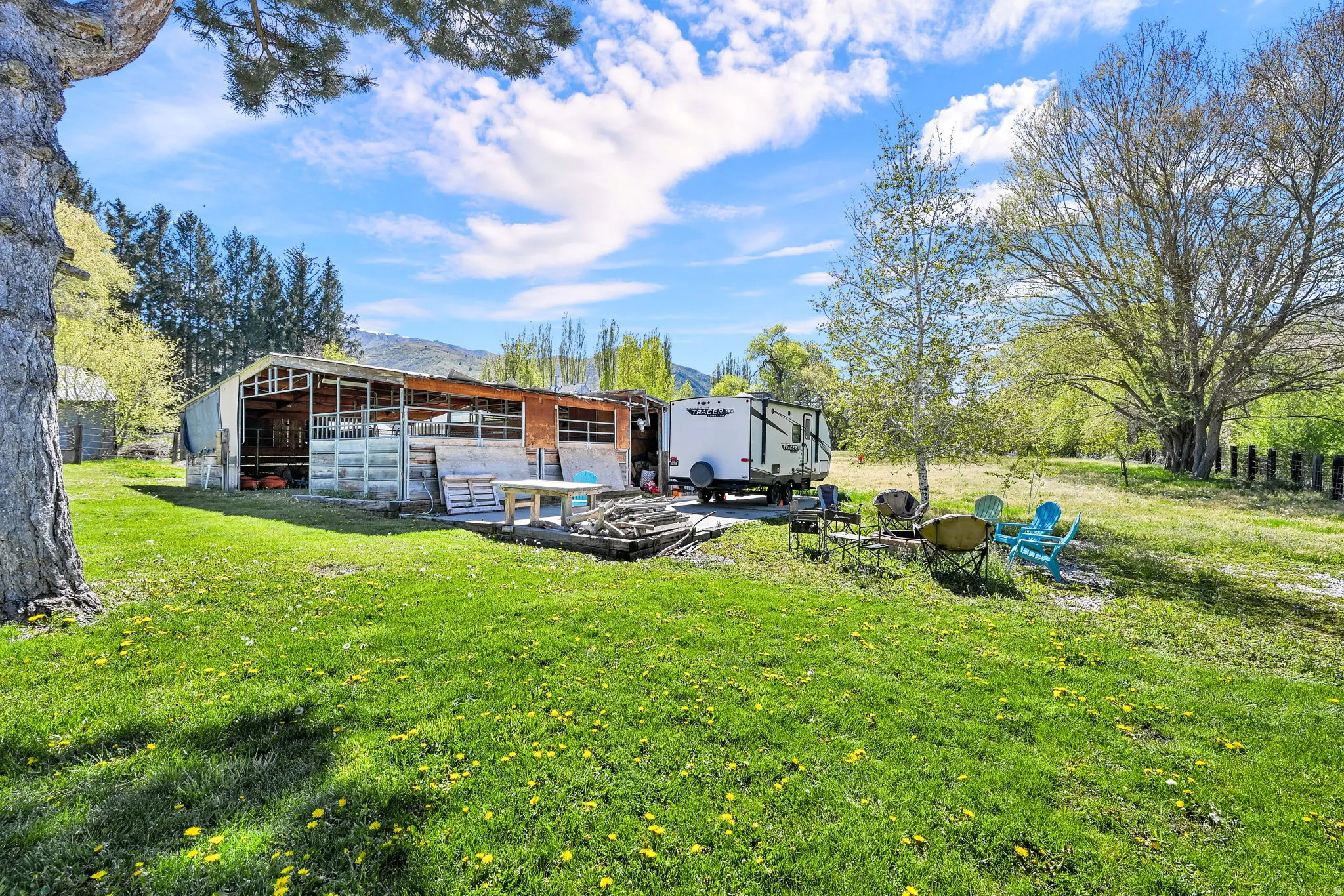 Expansive green space featuring a large outbuilding with a metal roof, a gravel parking area, and mature trees