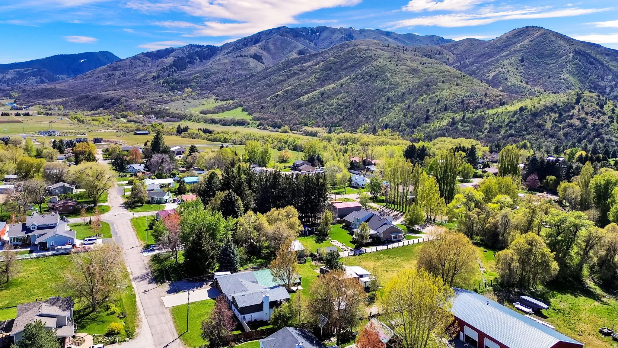 Expansive mountain range backdrop surrounding a verdant valley with residential properties and abundant mature trees