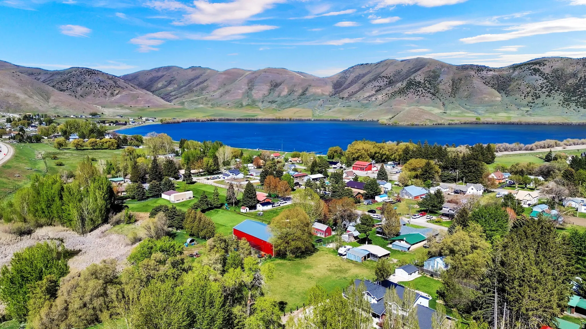 Aerial perspective showcasing a vibrant community nestled beside a large blue lake, with rolling hills and mountains forming a prominent backdrop
