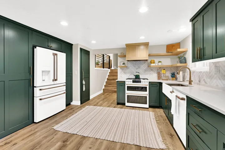 Modern kitchen featuring dark green cabinetry, white appliances, wood-finish flooring, white countertops, and a white subway tile backsplash. "Hidden pantry" door is located next to the fridge.  And GE Cafe appliances are included.