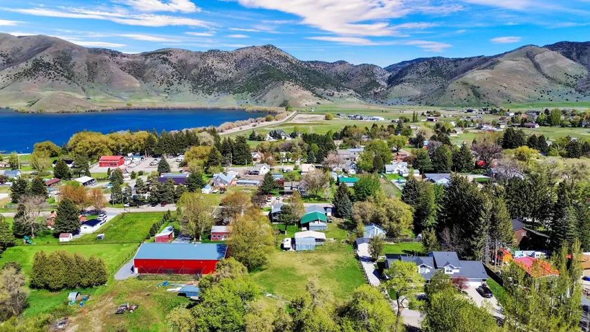 Expansive rural landscape featuring a large body of water, distant mountains, a collection of residential properties, verdant trees, and open green spaces