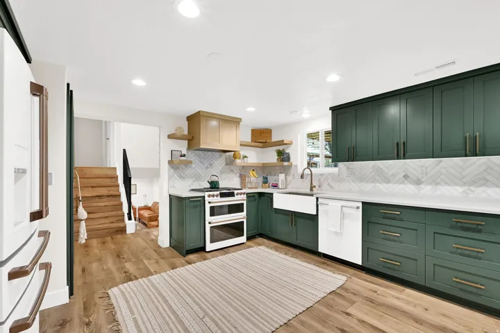 Modern kitchen featuring dark green cabinetry with brass-finish hardware, light wood-finish flooring, a white farmhouse sink, and herringbone pattern backsplash