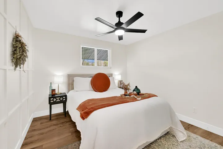 Bedroom with wood-finish flooring, a decorative accent wall, and a ceiling fan with integrated lighting