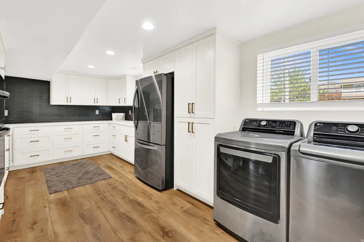 Hidden butler pantry with laundry area featuring wood-finish flooring, white cabinetry with gold-tone hardware, dark subway tile backsplash, and stainless steel appliances
