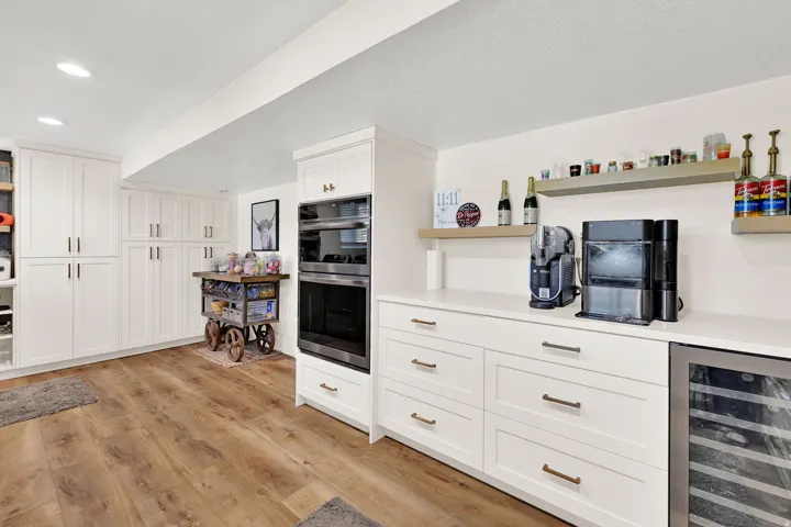 Hidden butler pantry with laundry area featuring wood-finish flooring, white cabinetry with gold-tone hardware, dark subway tile backsplash, and stainless steel appliances (wine cooler is included)