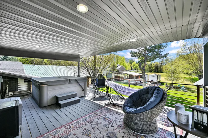 Covered outdoor deck featuring a hot tub, recessed lighting, and a horizontal slatted railing. Private entrance from primary suite.