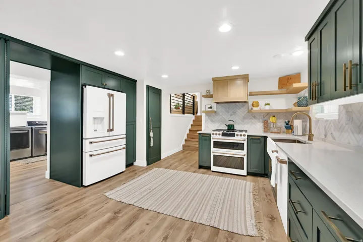 Modern kitchen featuring wood-finish flooring, dark green cabinetry, white countertops, and a white tile backsplash.  "Hidden pantry" door is located next to the fridge. And GE Cafe appliances are included.