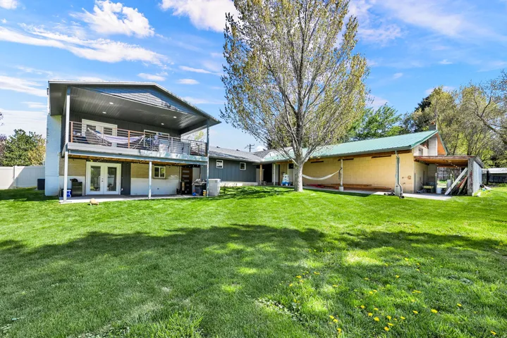 Expansive green lawn with mature tree, featuring a multi-level exterior with covered balcony, covered patio with French doors, and an additional single-story structure with covered exterior space
