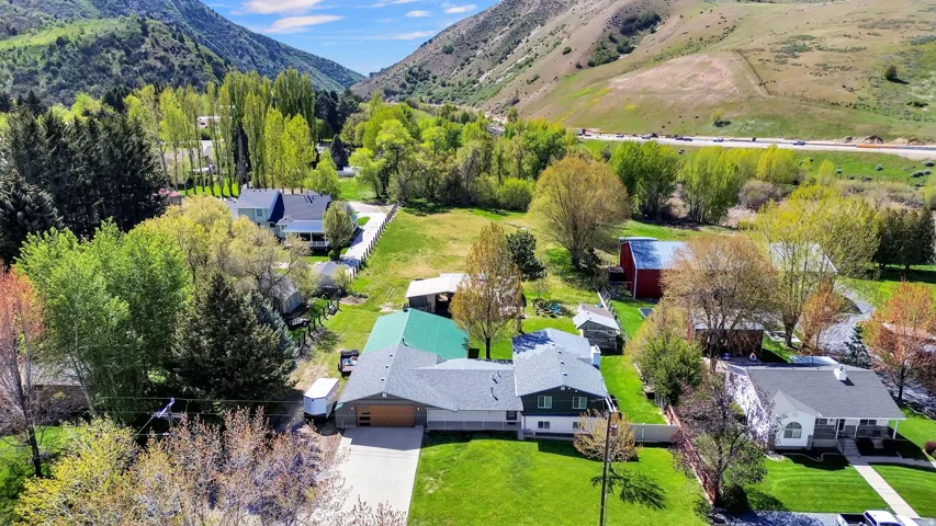Expansive property featuring a green metal roof, attached garage, well-maintained lawn, mature trees, and a mountain backdrop