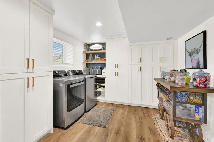Hidden butler pantry with laundry area featuring wood-finish flooring, white cabinetry with gold-tone hardware, dark subway tile backsplash, and stainless steel appliances (wine cooler is included)