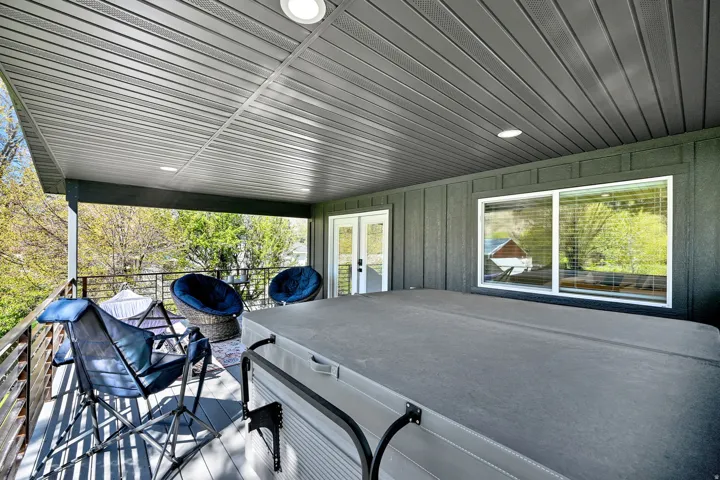 Covered outdoor deck featuring a hot tub, recessed lighting, and a horizontal slatted railing. Private entrance from primary suite.