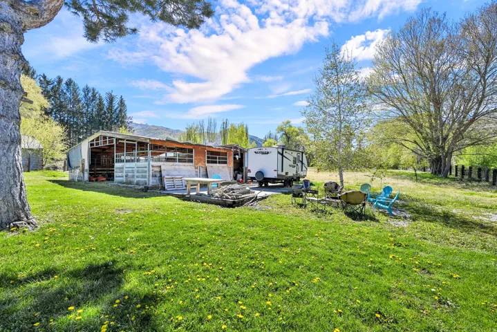 Expansive green space featuring a large outbuilding with a metal roof, a gravel parking area, and mature trees