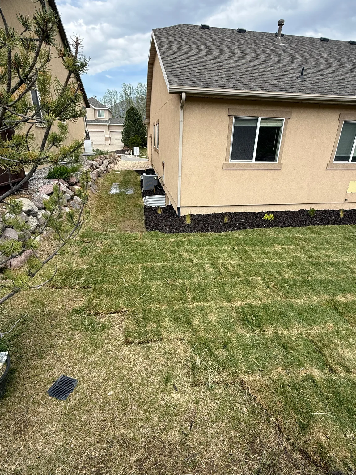 Side yard featuring newly installed sod, a rock retaining wall, and a garden bed with fresh mulch