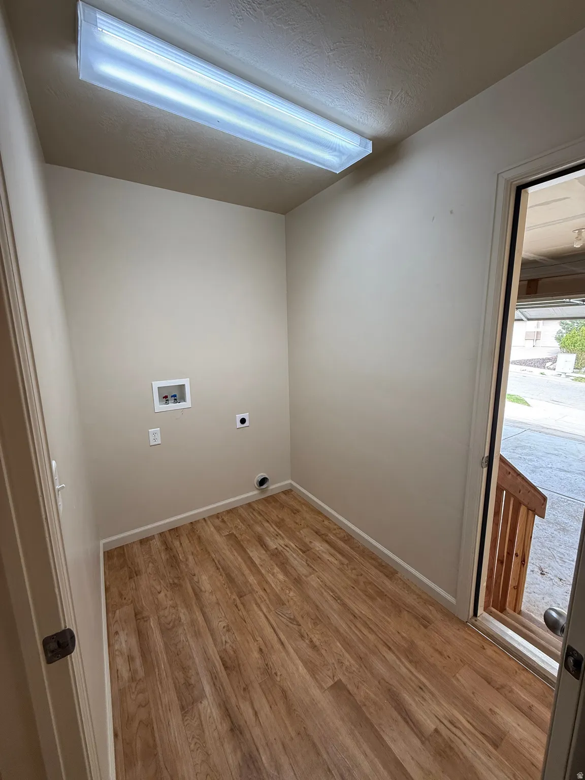 Dedicated laundry space featuring wood-finish flooring, neutral-toned walls, and a fluorescent ceiling light fixture