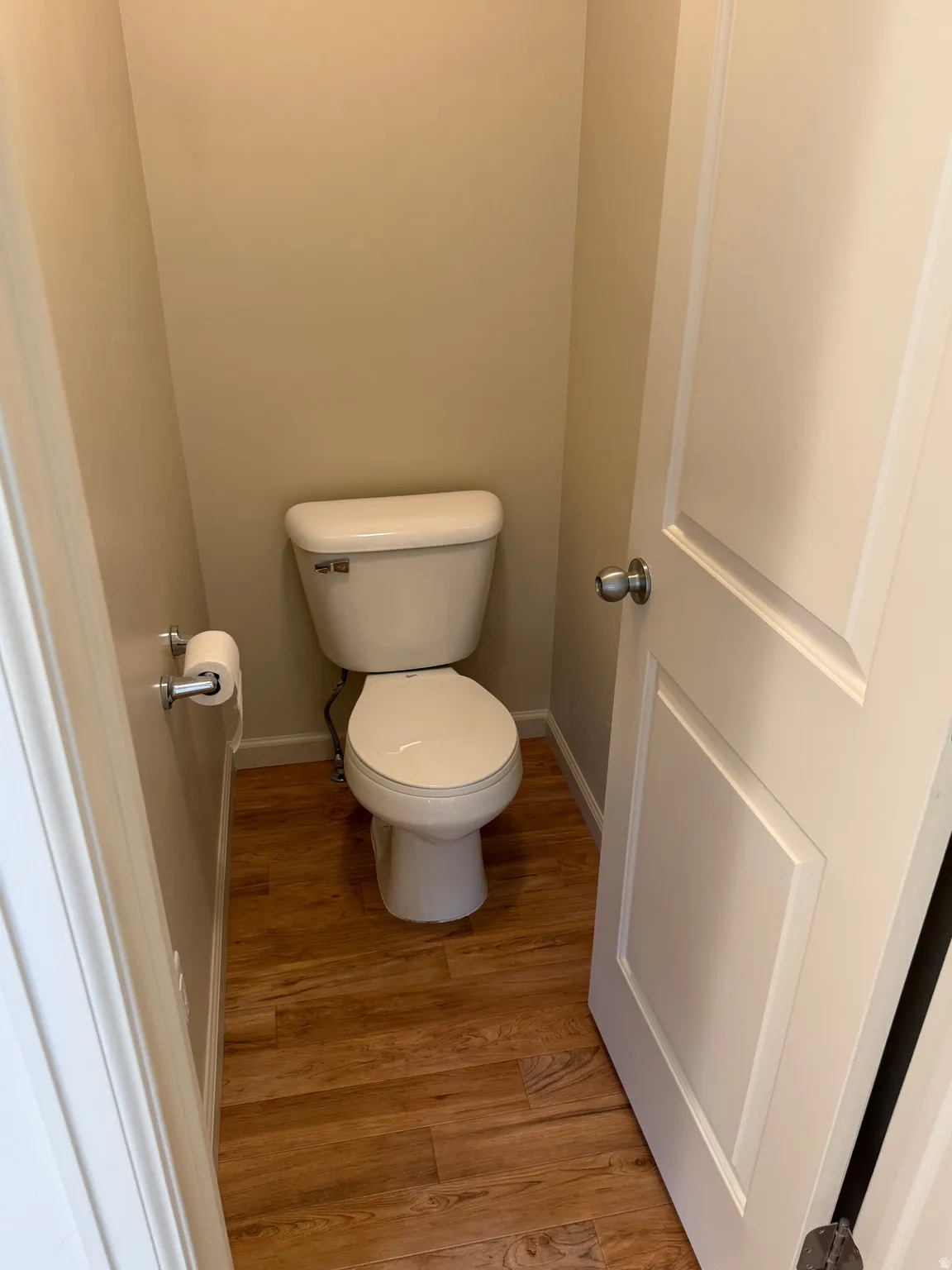 Powder room with a two-piece toilet, wood-finish flooring, and a white paneled door with a brushed nickel doorknob