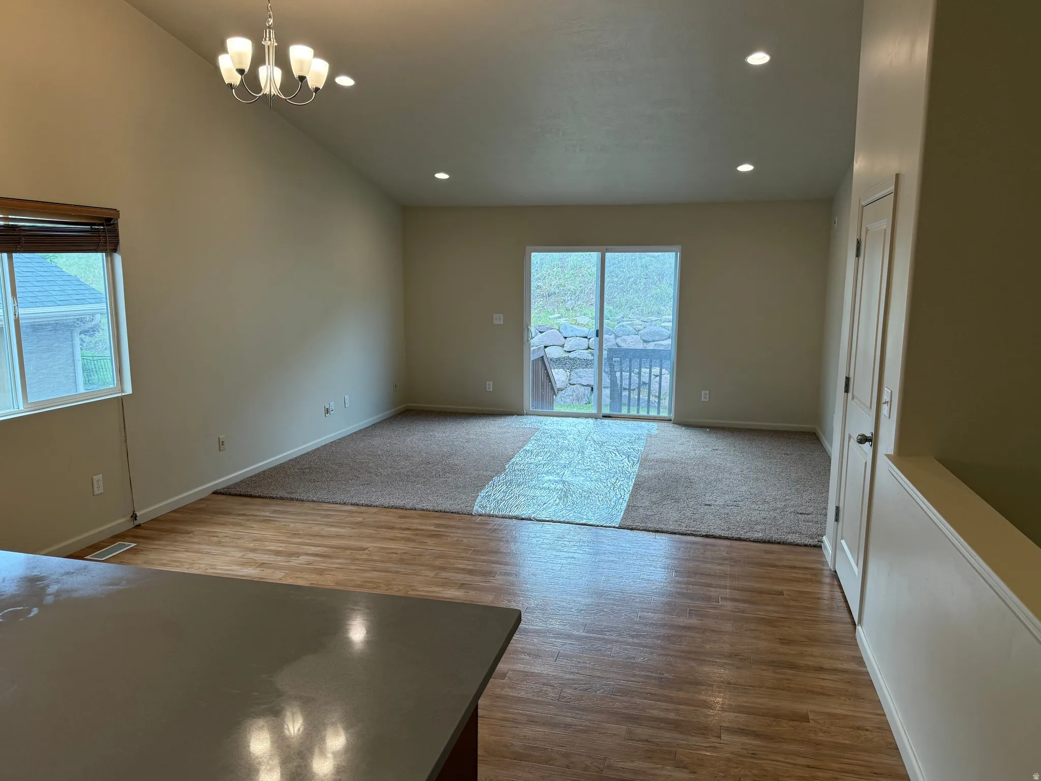 Open-concept living area featuring a vaulted ceiling and a mix of wood-finish flooring and carpet