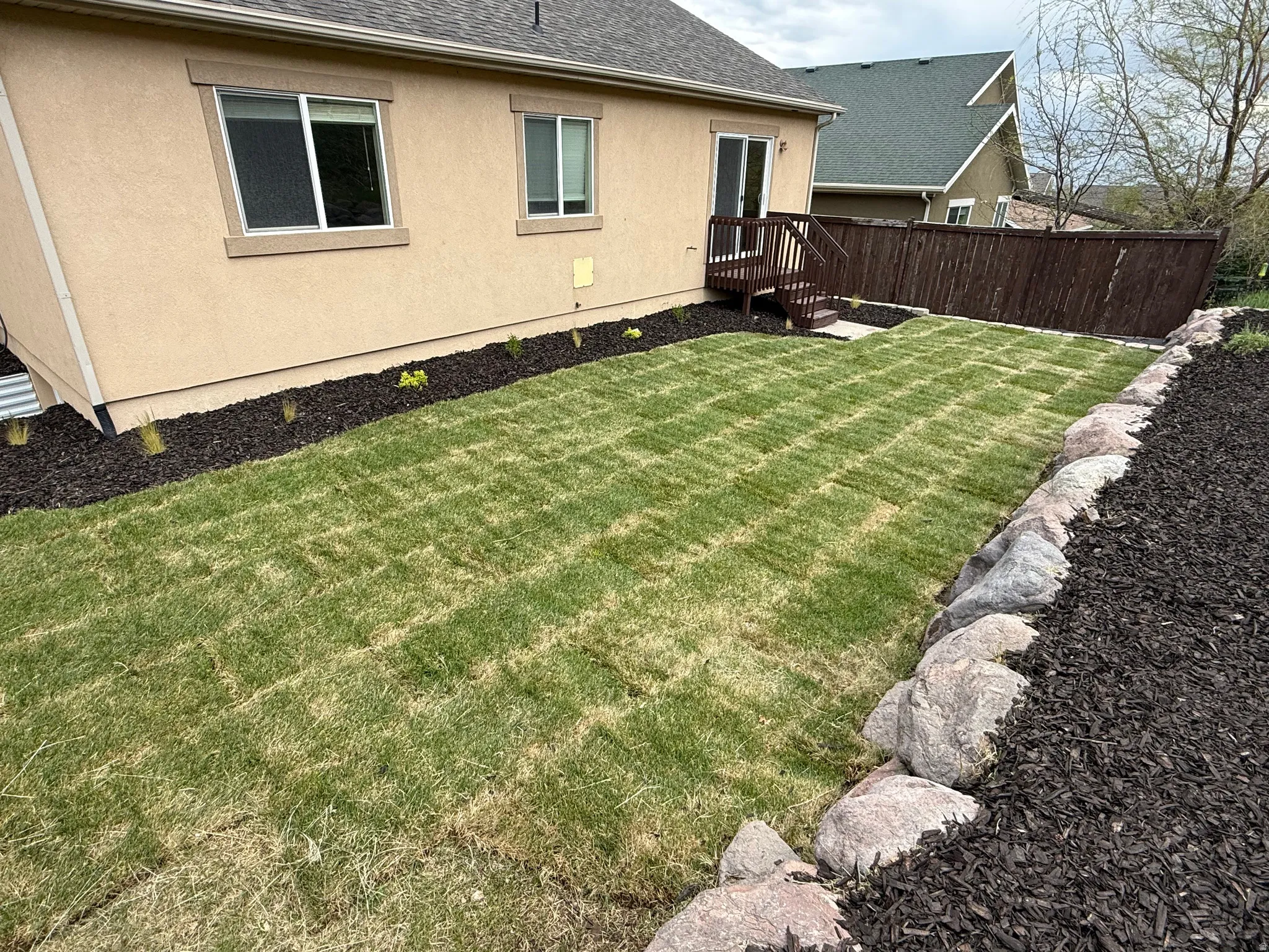 Rear exterior featuring a sliding glass door, elevated wood deck with stairs, new sod lawn, and a dark stained privacy fence