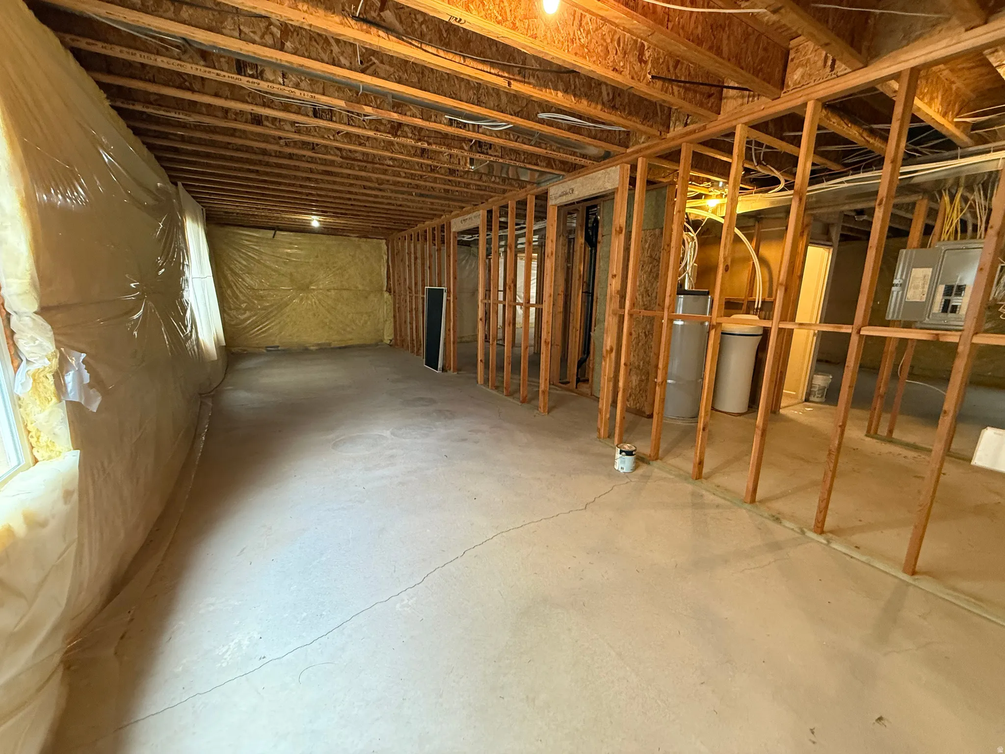 Unfinished basement featuring exposed wood framing, concrete flooring, and insulated walls