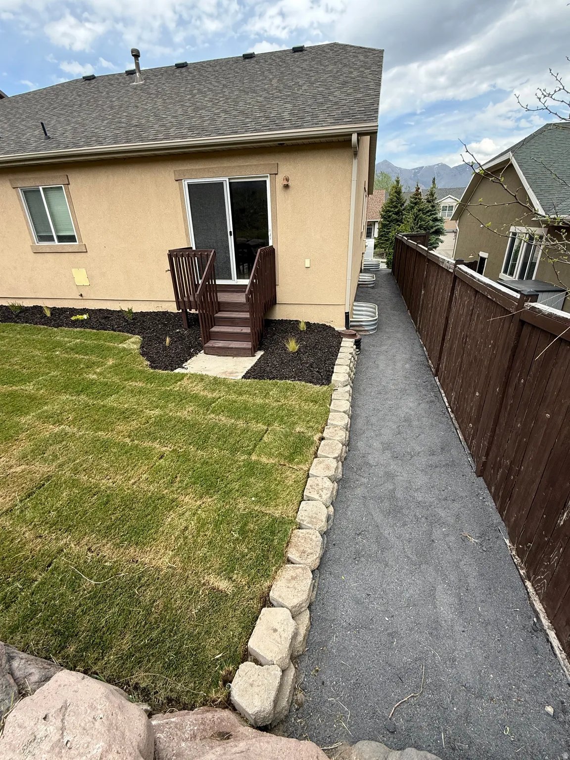 Rear exterior featuring a sliding glass door with a private deck and stairs, manicured lawn with landscape curbing, and a gravel pathway