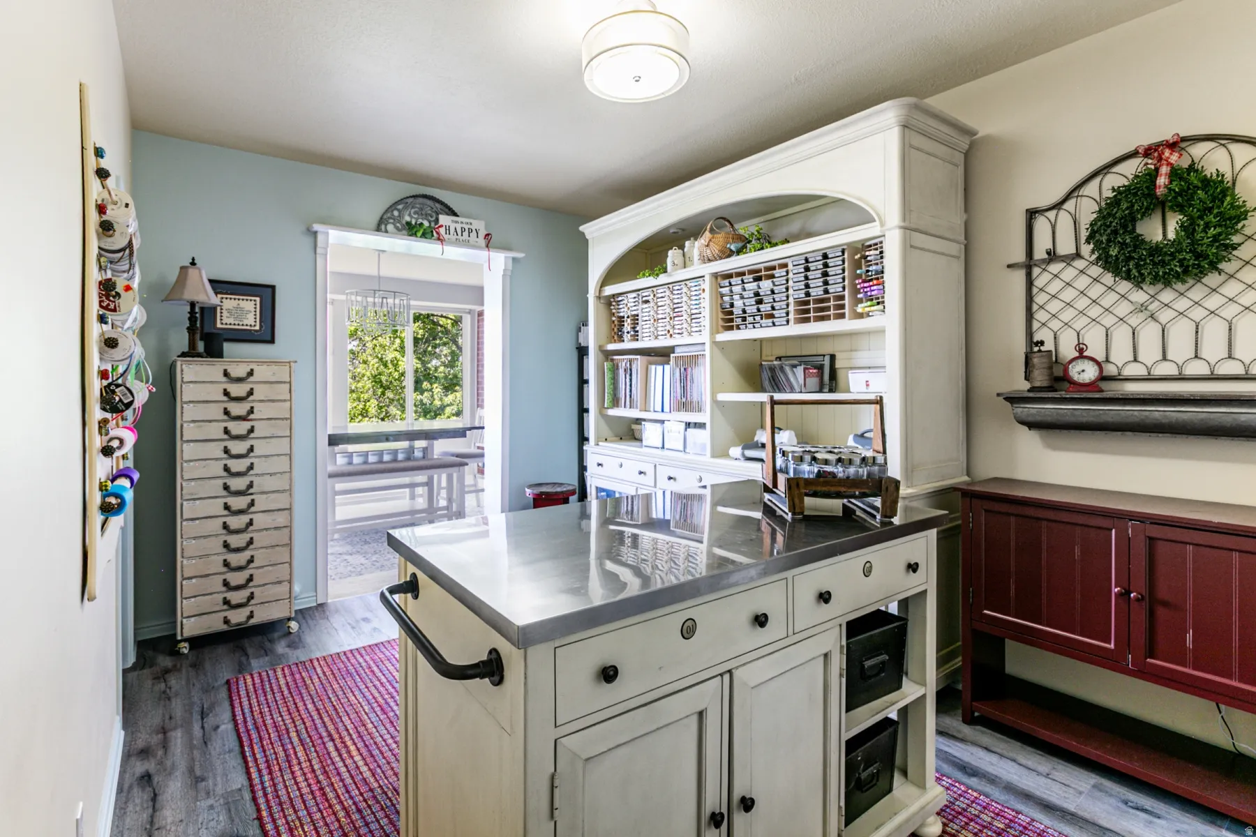 Versatile room featuring a central island with a metal countertop, extensive built-in shelving, distressed wood-finish flooring, and a large doorway opening to an outdoor area