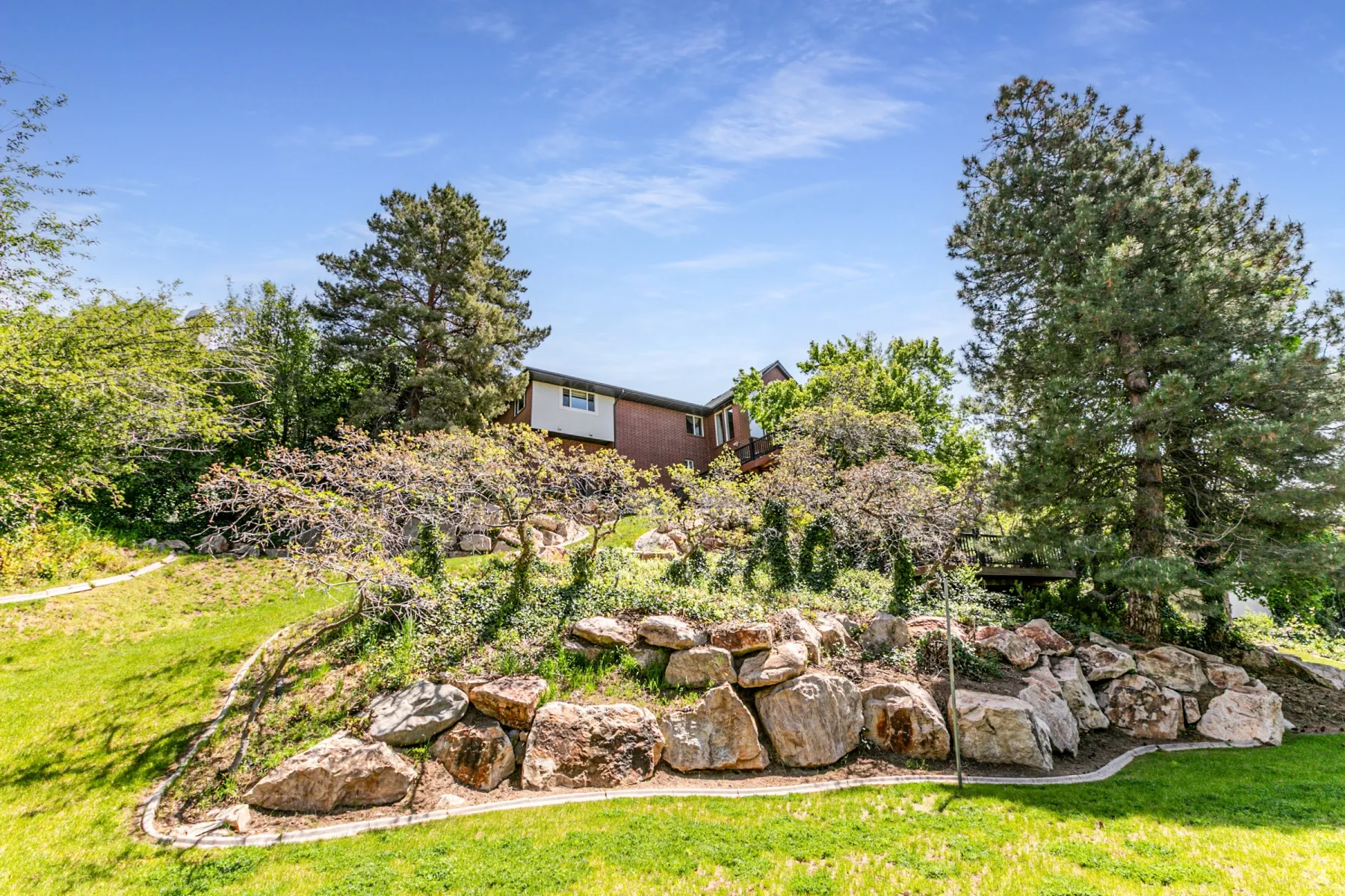 Terraced landscaping featuring large natural rock retaining walls, mature trees, and established shrubbery